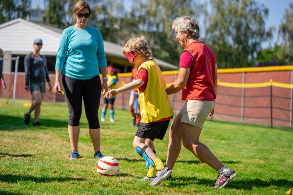 Young boy with eye shields playing soccer with two adults.