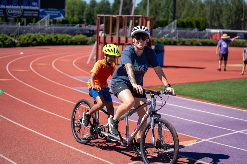 Tandem biking at Camp Spark with a counselor in front and the athlete in back.