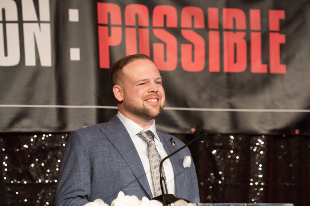 Billy presenting behind a microphone.